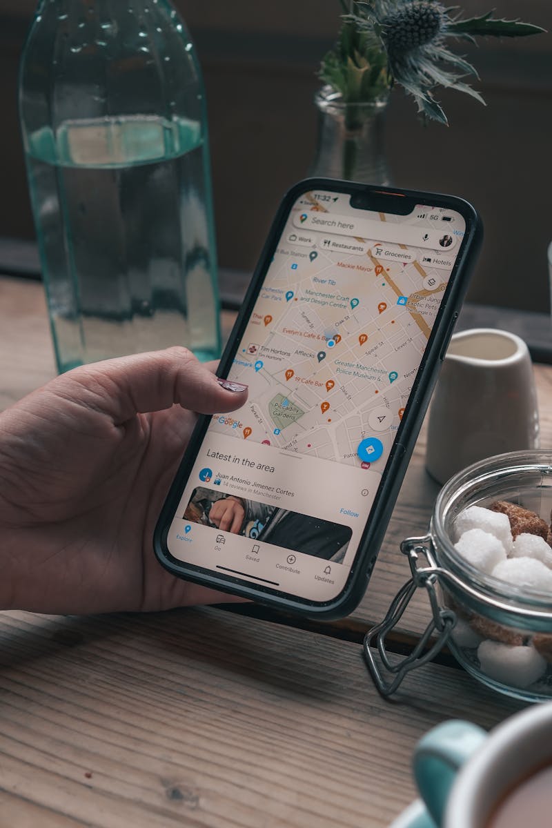 A hand uses a smartphone for navigation in a cozy Manchester cafe.